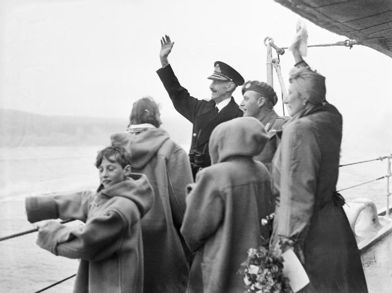 Photograph of the royal family waving to the welcoming crowds upon their return to Norway on June 7, 1945. Crown Prince Harald is at left, facing the camera. Collection of the Imperial War Museums, London. Photo by Lt. E. A. Zimmerman, Royal Navy official photographer, and courtesy of Wikimedia Commons.