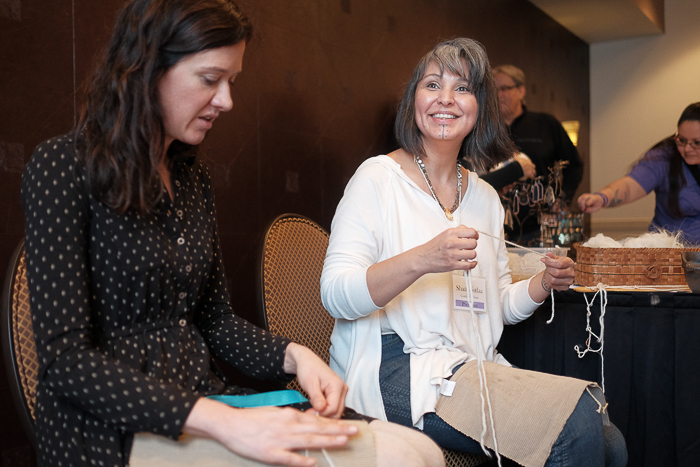 Shaa (right) teaches Ashli Tyre and other attendees the technique of thigh spinning at the Salish Wool Weaver's Symposium. Photo: Kathy Cadigan.